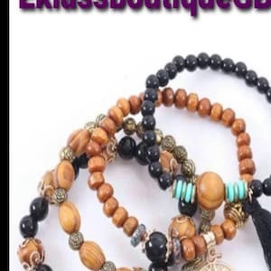 Puede incluir: Pulseras apiladas con cuentas de madera en tonos marrón y negro, acentuadas con cuentas y dijes de metal dorado. Una pulsera tiene un dije de árbol de la vida y cuentas turquesas. El texto "EklassboutiqueGB" está en la parte superior.