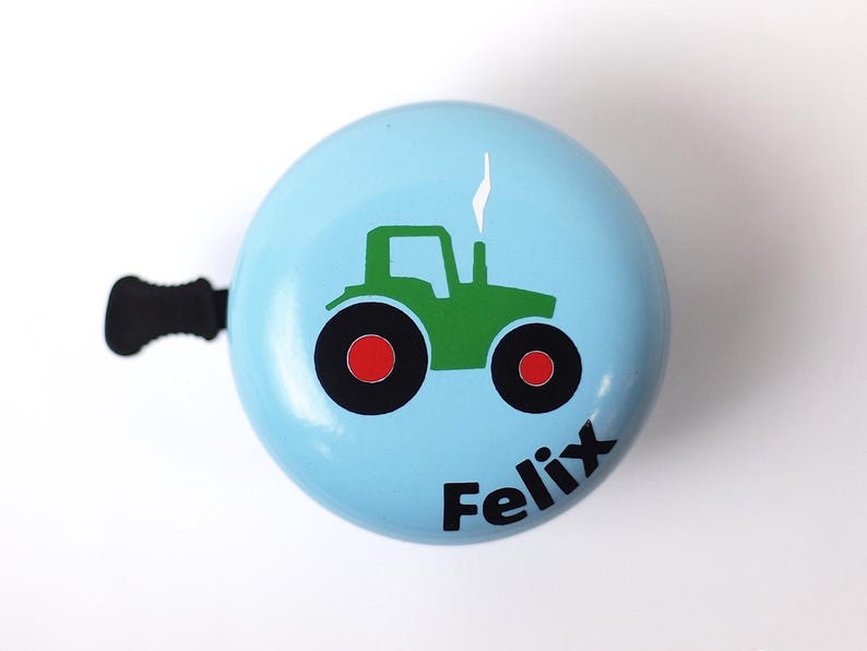 Peut inclure: Une sonnette de v&eacute;lo bleu clair avec un dessin de tracteur vert et le nom "Felix" imprim&eacute; sur le devant.
