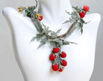 May include: A delicate necklace featuring a vine design with red berries and green leaves. The necklace is made of beads and is displayed on a white mannequin. The necklace also includes a pair of matching earrings with a red flower design.