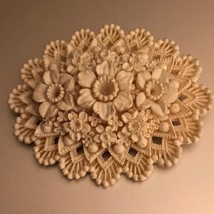 May include: A white, oval-shaped brooch with a floral design. The brooch is made of plastic and features a cluster of raised flowers with intricate details.