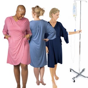 Puede incluir: Tres mujeres con batas suaves tipo envolvente en rosa, azul y marino. La bata rosa tiene cierre de lazo y bolsillos. Un soporte intravenoso médico está en el fondo. Las batas parecen estar hechas de una tela cómoda y ligera.
