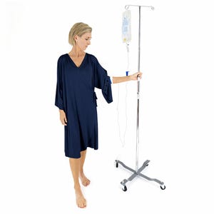 Puede incluir: Una bata envolvente azul marino con mangas tres cuartos. Un soporte de goteo cromado con una bolsa de líquido transparente está junto a la bata. El soporte tiene una base con ruedas para facilitar el movimiento.