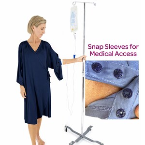 Puede incluir: Bata envolvente azul marino con mangas con botones a presión para acceso médico. La bata tiene cuello en V y mangas largas con detalles de botones. Un primer plano muestra el cierre de botón a presión en la manga. El texto "Snap Sleeves for Medical Access" es visible.