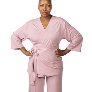 May include: A woman wearing a pink, long-sleeved, wrap-style top and matching pants. The top has a V-neck and a tie belt. The pants have a straight leg.