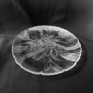May include: A clear glass serving plate with a decorative floral design. The plate has a scalloped edge and is perfect for serving appetizers, desserts, or snacks.