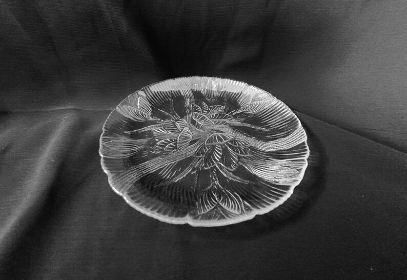 May include: A clear glass serving plate with a decorative floral design. The plate has a scalloped edge and is perfect for serving appetizers, desserts, or snacks.