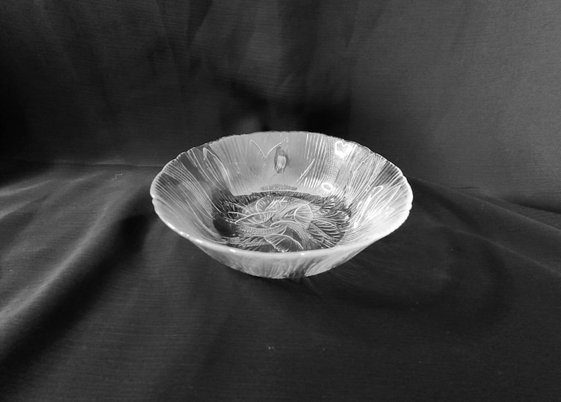 May include: A clear glass bowl with a decorative floral pattern. The bowl is empty and sitting on a black surface.