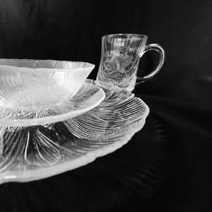 May include: A set of clear glass dishes with a delicate floral pattern. The set includes a bowl, a plate, and a mug.