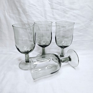 May include: Four clear glass wine glasses with a smoky gray tint. The glasses are arranged in a group, with one glass lying on its side.