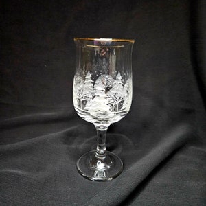 May include: A clear glass wine glass with a gold rim and a white etched design of a winter scene with trees and snowflakes.