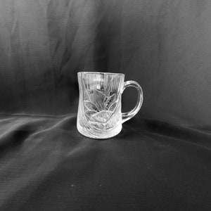May include: A clear glass mug with a decorative etched design. The mug has a handle and is perfect for serving beverages.