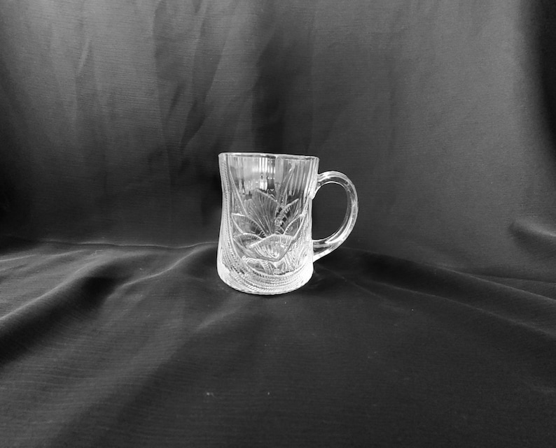 May include: A clear glass mug with a decorative etched design. The mug has a handle and is perfect for serving beverages.