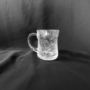 May include: A clear glass mug with a decorative etched design. The mug has a handle and a wide base.