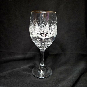May include: A clear glass wine glass with a gold rim and a white etched design of snow-covered trees.