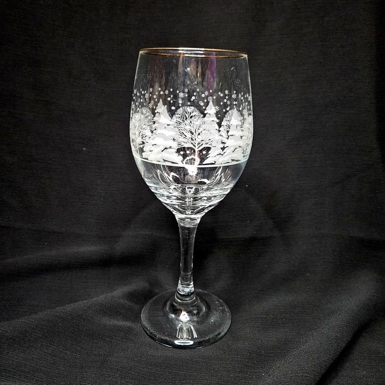 May include: A clear glass wine glass with a gold rim and a white etched design of snow-covered trees.