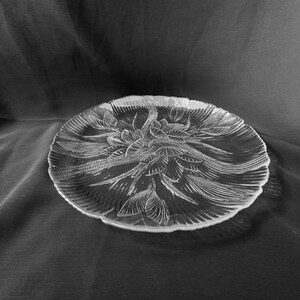 May include: A clear glass serving platter with a decorative floral design. The platter has a scalloped edge and is perfect for serving appetizers, desserts, or other snacks.