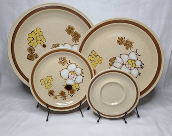 Puede incluir: Juego de cuatro platos de cena de cerámica marrón y beige con un diseño floral. Los platos presentan flores amarillas, blancas y rosas con tallos y hojas marrones.