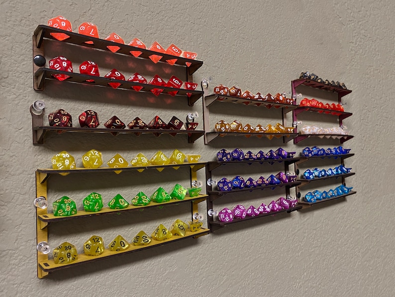 May include: A wall-mounted wooden shelf unit with multiple shelves displaying a collection of colourful dice. The dice are arranged in rows on each shelf, with different colours and patterns. The shelves are made of wood and have a natural finish.