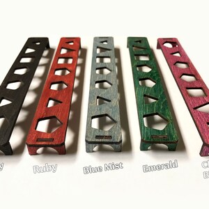 May include: Five wooden dice trays in different colours: ebony, ruby, blue mist, emerald, and cherry blossom. Each tray has seven slots for dice.