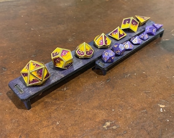 May include: A wooden dice tray with two rows of purple and gold dice. The dice are numbered 1-20. The tray is made of dark wood and has a purple stain.