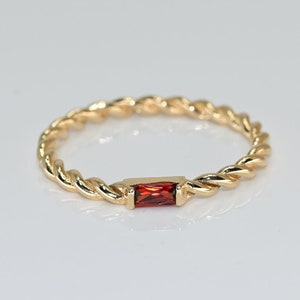 May include: A gold twisted band ring with a single red gemstone.