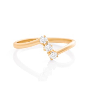 May include: A gold-colored ring with three clear, round gemstones set in a curved design. The ring's band is smooth and polished, and the gemstones are evenly spaced along the curve. The ring is set against a white background.