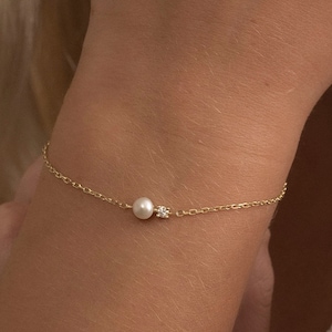 May include: A delicate gold chain bracelet with a single pearl and a small diamond accent.
