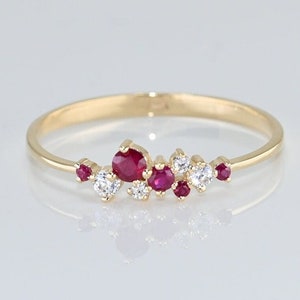May include: A delicate gold band ring with a cluster of small red rubies and white diamonds set in a scattered pattern.