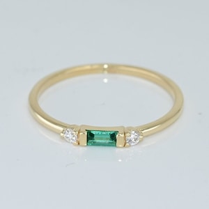 May include: A gold band ring with a green emerald gemstone and two small diamonds.