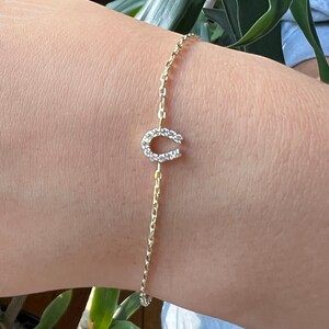 May include: A gold chain bracelet with a horseshoe charm set with clear cubic zirconia stones.