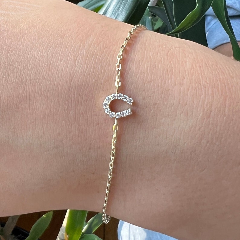 May include: A gold chain bracelet with a horseshoe charm set with clear cubic zirconia stones.