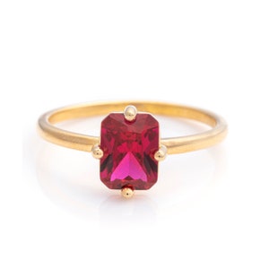 May include: A gold ring with a red emerald-cut gemstone.