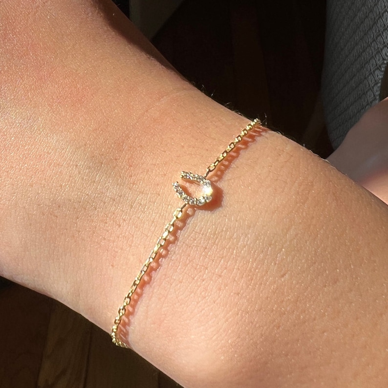May include: A gold chain bracelet with a horseshoe charm set with clear cubic zirconia stones.