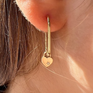Peut inclure: Boucles d'oreilles créoles en or avec un pendentif en forme de cœur orné d'un petit diamant. Les boucles d'oreilles sont d'un design simple et élégant.