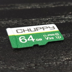 May include: A green and white 64GB CHUPPY Class 10 V30 SD card. The card has the text "CHUPPY" in white, and "64 GB" in white. The card is on a black surface.