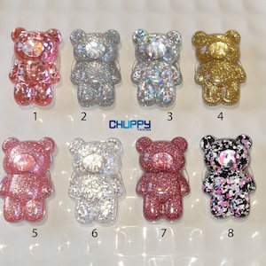 May include: Eight glitter bear-shaped phone grips in shades of pink, silver, gold, and black. Each bear features a central gem and a clear adhesive backing. The text "CHUPPY TECH" is displayed.