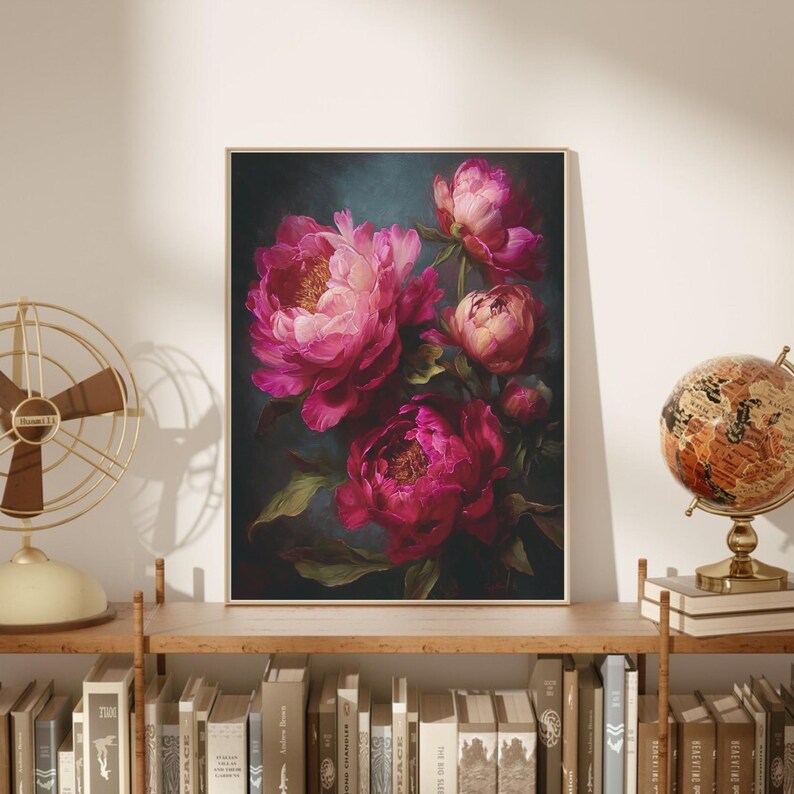 May include: A framed floral print featuring a bouquet of vibrant pink peonies against a dark teal background. The painting has a soft, painterly style with visible brushstrokes. The artwork is displayed on a wooden shelf with books and decorative items.