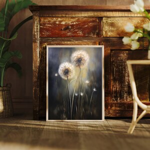 May include: A framed artwork featuring a close-up of dandelions. The painting showcases two large, fluffy dandelion seed heads with delicate stems against a dark, blurred background. The artwork is displayed on a wooden floor.