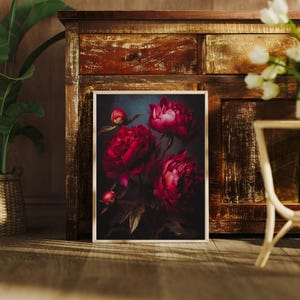May include: A framed floral print featuring vibrant red peonies against a dark background. The artwork showcases the flowers in full bloom, with detailed petals and green leaves. The print is displayed on a wooden floor, leaning against a rustic cabinet.