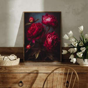 May include: A framed floral print featuring vibrant red peonies against a dark background. The artwork showcases the flowers in full bloom, with detailed petals and green leaves. The print is displayed on a wooden surface, with a vase of white tulips nearby.