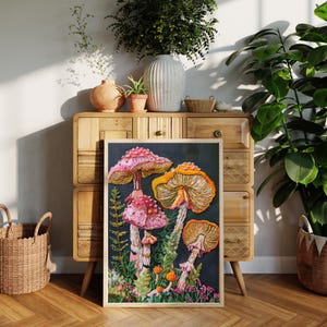 Puede incluir: Una impresi&oacute;n de arte enmarcada que presenta un primer plano de cuatro hongos vibrantes de color rosa y naranja con manchas blancas, rodeados de follaje verde y peque&ntilde;as flores rosas sobre un fondo oscuro.
