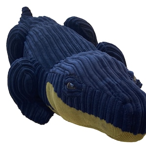 Op de afbeelding: Een pluche blauwe alligator speelgoed met een gele buik en zwarte ogen. De alligator is gemaakt van een zachte, textuurrijke stof.