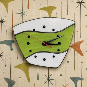 May include: A trapezoidal wall clock made of stained glass with a wavy design featuring white and lime green sections. The clock face has black circular hour markers and black hour and minute hands, with a thin red second hand at the center.