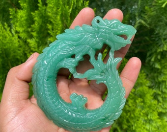 Puede incluir: Un colgante de jade verde tallado en forma de dragón enroscado. La cabeza del dragón está mirando hacia adelante con la boca abierta. El colgante está detallado con escamas y garras.