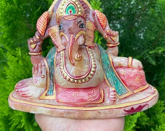 May include: A hand-painted, pink and white stone statue of Ganesha, the Hindu god of wisdom and prosperity. The statue is decorated with gold paint and features intricate details.