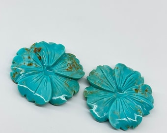 May include: Two turquoise blue flower-shaped cabochons with brown veining. The cabochons are carved from turquoise and have a smooth, polished finish.