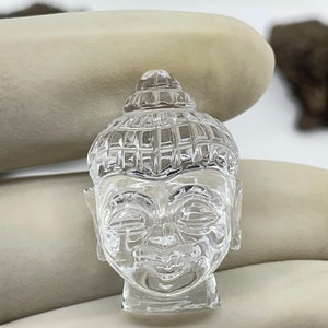 Puede incluir: Una escultura de cabeza de Buda de cristal transparente con una expresión serena. La escultura está tallada con detalles intrincados y tiene un acabado liso y pulido.