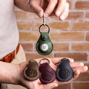 May include: Four leather keychains with different designs. One keychain has an apple logo, one has the initials "CTR" with a laurel wreath, one has the initials "HL" in a square, and one has the initials "SB" in a circle.