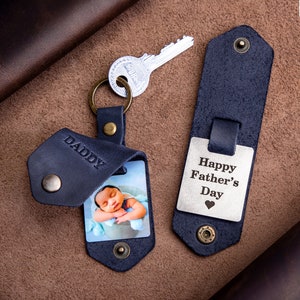 May include: A blue leather keychain with a photo insert and the word "Daddy" engraved on it. The keychain also includes a silver key ring and a separate blue leather tag with the text "Happy Father's Day" engraved on it.