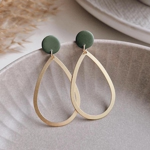 Op de afbeelding: Een paar gouden traanvormige oorbellen met een groene ronde hanger die aan elke oorbel hangt.